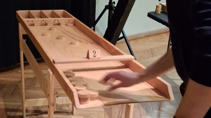 Shuffleboard/Jakkolo im Spiel – eine Hand nimmt Pucks aus der Auffangschale