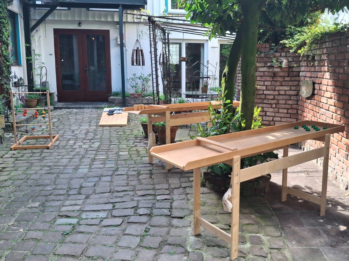 Aufbau im Innenhof: Leitergolf, Cornhole und Holz-Spieltische auf dem Kopfsteinpflaster