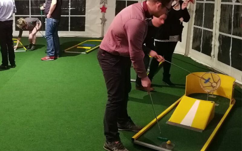 Gast spielt bei einer Firmenfeier im Zelt auf einer mobilen Minigolfbahn